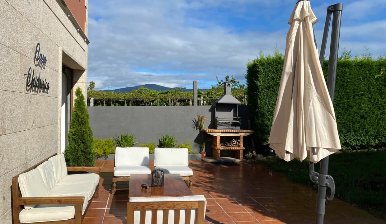 Jardín con barbacoa, sofás y sombrilla